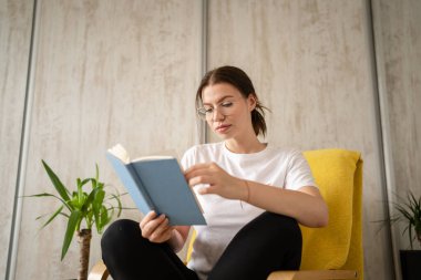 One woman young adult caucasian female sitting in chair at home read book copy space front view real people leisure weekend concept looking to the book thinking contemplate