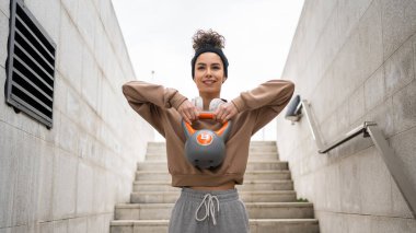 Kafkasyalı genç bir bayan sporcu gün içinde dışarıda Rus çanı Girya Kettlebell ağırlık egzersizi ile antrenman yapıyor.