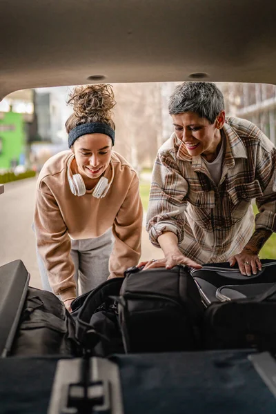 2人の美しい女性学生の母親と娘の女性旅行のコンセプトは 大学のキャンパスや旅行の寮に移動しながら 車の後ろから荷物スーツケースやその他のものを取ります — ストック写真