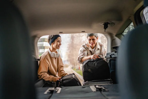 2人の美しい女性学生の母親と娘の女性旅行のコンセプトは 大学のキャンパスや旅行の寮に移動しながら 車の後ろから荷物スーツケースやその他のものを取ります — ストック写真