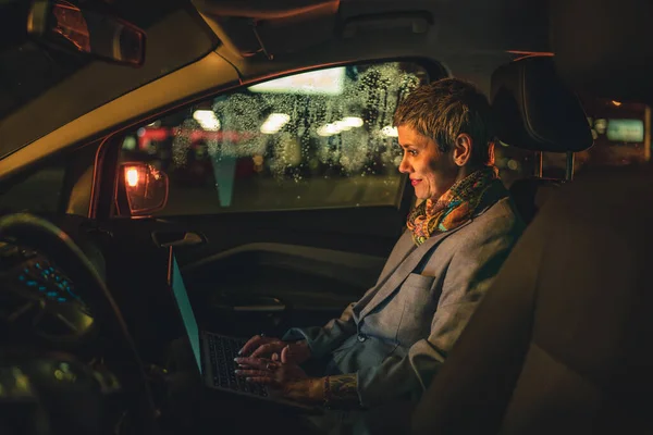 1人の成熟したシニア女性白人女性が夜の暗闇の中でラップトップコンピュータで働いている車の中で座っています短い灰色の髪の現代的なマネージャーまたは道路コピースペースのビジネス所有者 — ストック写真