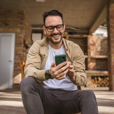 Beyaz tenli, sakallı ve gözlüklü bir adam güneşli bir günde açık havada oturur. Tişört giyer, cep telefonu kullanır. SMS mesajları atar, internete girer, internetten arama yapar.