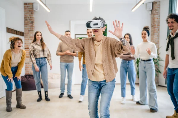 stock image One woman mature senior caucasian female in front of group of men and women friends enjoy virtual reality VR headset at work having fun together during team building seminar real people bright filter