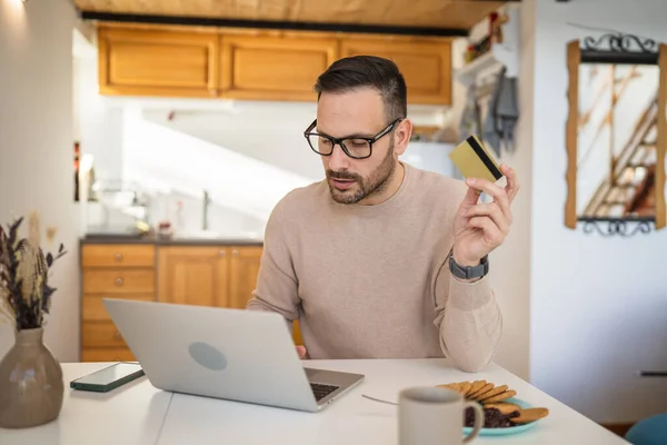 一个成熟的男性男子坐在家里开心地笑着用笔记本电脑拿着银行卡在线购物网上购物网上购物概念真实的人抄袭空间电子商务网上银行服务 — 图库照片