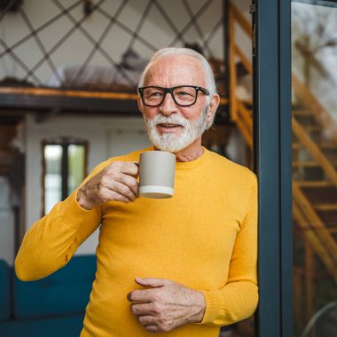 Yaşlı, beyaz, sakallı ve gözlüklü bir adam gün içinde balkonda mutlu bir gülümseme içinde kahvenin fotokopi makinesinin günlük konseptini tutuyor.