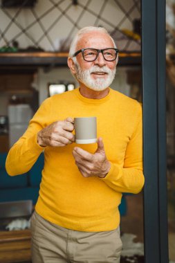 Yaşlı, beyaz, sakallı ve gözlüklü bir adam gün içinde balkonda mutlu bir gülümseme içinde kahvenin fotokopi makinesinin günlük konseptini tutuyor.