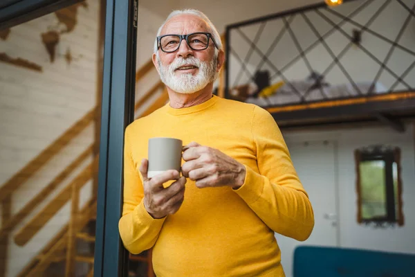 stock image One man senior caucasian male with beard and eyeglasses stand on balcony at door in day happy smile hold cup of coffee copy space morning daily routine concept