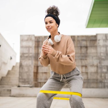 Bir yetişkin beyaz kadın sporcu şehrin dışında esmer ve sağlıklı esmer kadınlar için esneme konseptinde esnemiş beton arka planda elastik lastik direnç bantları ile eğitim görüyor.