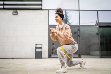 Bir yetişkin beyaz kadın sporcu şehrin dışında esmer ve sağlıklı esmer kadınlar için esneme konseptinde esnemiş beton arka planda elastik lastik direnç bantları ile eğitim görüyor.