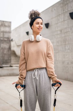 Yetişkin bir kadın beyaz kadın sporcu elastik lastik direnç bantları ile antrenman yapıyor. Şehrin dışında çimento arka planda esmer, sağlıklı ve zinde esnek esneme konseptini taklit ediyor.