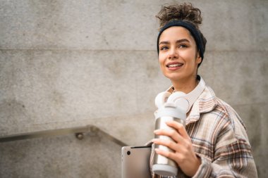 Genç bir kadın yetişkin kız öğrenci ayakta duruyor ya da dışarıda yürüyor dizüstü bilgisayar ve bir fincan kahve tutuyor gerçek bir insan uzayı kopyalıyor mutlu bir gülümseme kulaklıkla gün içinde kendine güveniyor.