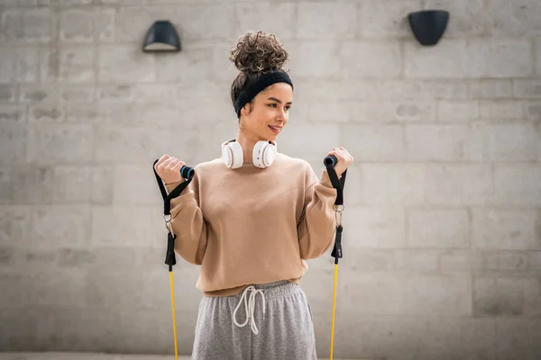 一名成年女子高加索女运动员在城市室外接受了弹性橡皮筋试管的训练 其背景为混凝土背景 伸展在快乐的黑发健康与健康的概念复制空间中 — 图库照片