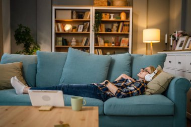 Yetişkin bir yaşlı beyaz kadın internet rehberli meditasyon için kulaklık kullanıyor. Farkındalık yogası yapıyor. Evde gözleri kapalı.