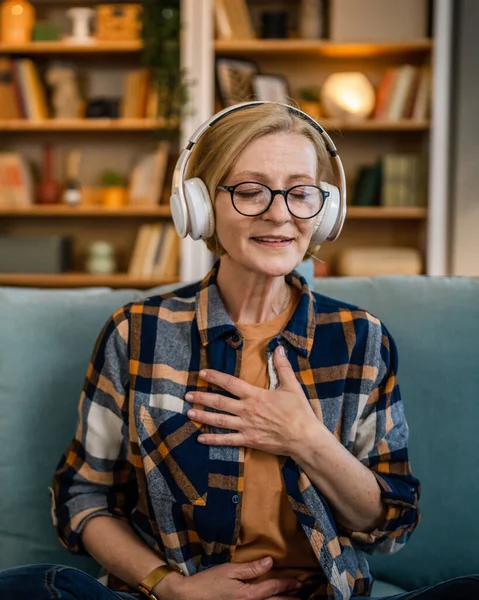 自宅で目を閉じてマインドフルネスヨガの症状を練習するオンラインガイド付き瞑想のためのヘッドフォンを使用して1人の女性成熟したシニア白人女性セルフケアコンセプトコピースペース — ストック写真