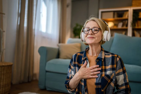 自宅で目を閉じてマインドフルネスヨガの症状を練習するオンラインガイド付き瞑想のためのヘッドフォンを使用して1人の女性成熟したシニア白人女性セルフケアコンセプトコピースペース — ストック写真