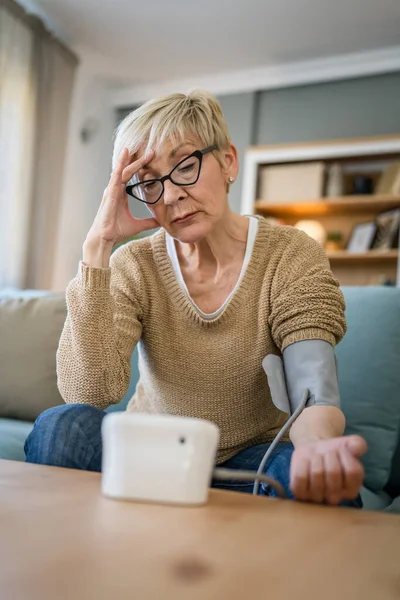 One woman senior caucasian female use blood pressure device on hand to check health results while sit at home real people health care concept worried bad results