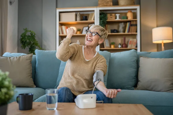 1人の女性高齢者原因アジアの女性は 自宅に座っている間に健康結果を確認するために手に血圧デバイスを使用しています実際の人々の健康管理の概念健康的なお祝い良い結果笑顔 — ストック写真