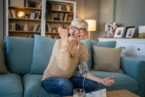 1人の女性高齢者原因アジアの女性は 自宅に座っている間に健康結果を確認するために手に血圧デバイスを使用しています実際の人々の健康管理の概念健康的なお祝い良い結果笑顔 — ストック写真