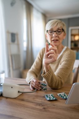 Yaşlı bir beyaz kadın ilaç kullanıyor ya da evde vitamin takviyesi alıyor. Gerçek insanlar sağlık hizmetleri kavramı.