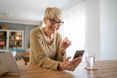 Kafkasyalı yaşlı bir kadın ilaç ya da vitamin takviyesi için evde bir bardak su içen bir kadın internet üzerinden gerçek insanların sağlık hizmetleri konseptini arıyor.