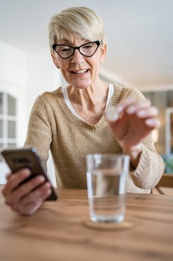 Yaşlı bir beyaz kadın ilaç ya da vitamin takviyesi hapı alıyor. Bir bardak suya koyuyor. Gerçek sağlık hizmetleri konseptinde tedaviyi hazırlıyor.