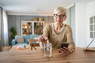 Yaşlı bir beyaz kadın ilaç ya da vitamin takviyesi hapı alıyor. Bir bardak suya koyuyor. Gerçek sağlık hizmetleri konseptinde tedaviyi hazırlıyor.
