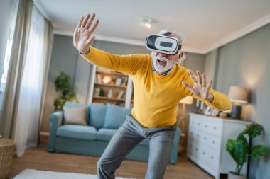 Yetişkin, yaşlı, beyaz bir erkek evde sanal gerçekliğin tadını çıkarıyor.