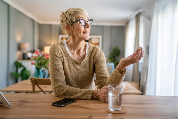 高齢の白人女性の1人が薬を服用するか または自宅で水のガラスとビタミンの発酵タブレットを補う実際の人々の健康管理コンセプト — ストック写真