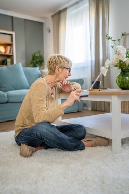 Yetişkin bir yaşlı kadın büyükanne evde oturup online alışveriş siteleri için kredi kartı ya da banka kartı kullanıyor. Bir şeyler satın alıyor. Dijital tablet kullanıyor. Gerçek insanlar yer kopyalıyor.