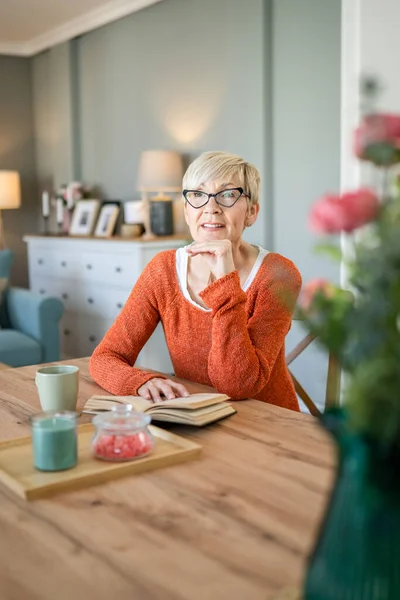 一位年富力强的老年女性退休老人是位成熟的女性 她是位现代祖母 留着短发 在家里看书 戴着眼镜 真实地复制着空间 — 图库照片