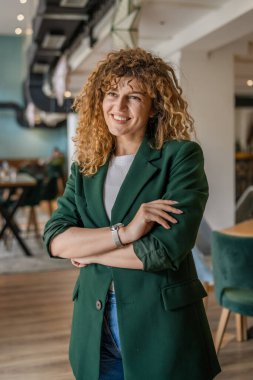 Kafkasyalı bir kadın kendine güveni tam, kafenin içinde kıvırcık saç portresiyle duruyor, gülümsüyor, gerçek bir insan mekanı kopyalıyor.