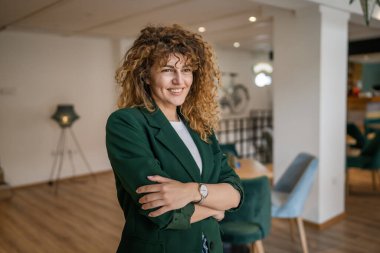 Kafkasyalı bir kadın kendine güveni tam, kafenin içinde kıvırcık saç portresiyle duruyor, gülümsüyor, gerçek bir insan mekanı kopyalıyor.