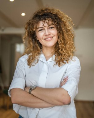 Kafkasyalı bir kadın kendine güveni tam, kafenin içinde kıvırcık saç portresiyle duruyor, gülümsüyor, gerçek bir insan mekanı kopyalıyor.