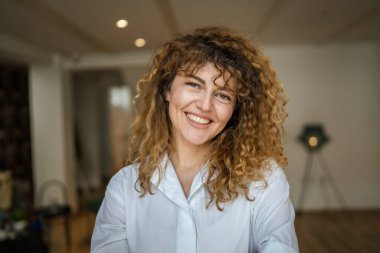 Kafkasyalı bir kadın kendine güveni tam, kafenin içinde kıvırcık saç portresiyle duruyor, gülümsüyor, gerçek bir insan mekanı kopyalıyor.