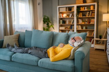 Yetişkin bir beyaz erkek internet rehberli meditasyon için kulaklık kullanıyor evde gözleri kapalı yoga tezahürü yapıyor gerçek insanların kişisel bakım kavramını taklit ediyor.