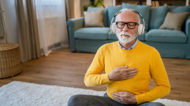 Yetişkin bir beyaz erkek internet rehberli meditasyon için kulaklık kullanıyor evde gözleri kapalı yoga tezahürü yapıyor gerçek insanların kişisel bakım kavramını taklit ediyor.