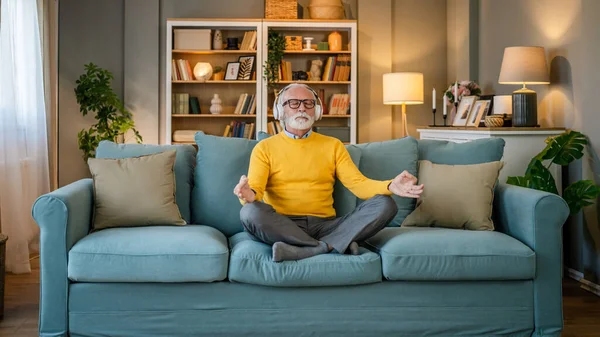 Yetişkin bir beyaz erkek internet rehberli meditasyon için kulaklık kullanıyor evde gözleri kapalı yoga tezahürü yapıyor gerçek insanların kişisel bakım kavramını taklit ediyor.