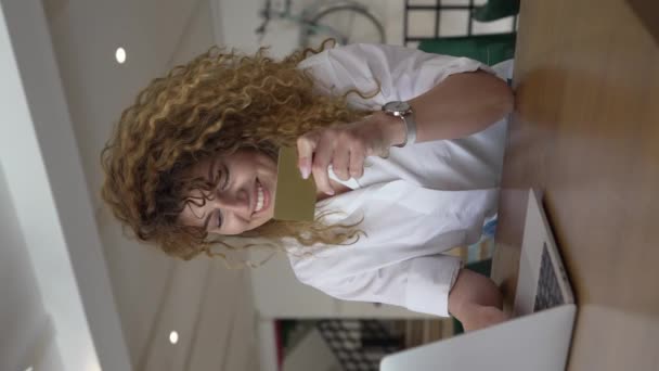 一位头发卷曲 面带笑容的女性成年人在网吧的笔记本电脑上用信用卡购物真人真事网上银行网上销售复制空间积极的情绪 — 图库视频影像