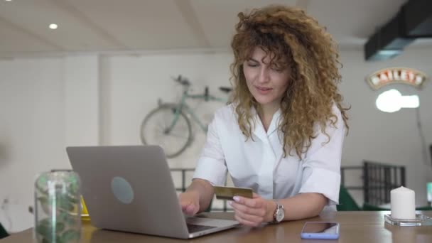 一位头发卷曲 面带笑容的女性成年人在网吧的笔记本电脑上用信用卡购物真人真事网上银行网上销售复制空间积极的情绪 — 图库视频影像
