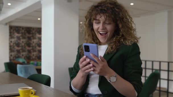 一位女性成人白种人卷发女用手机在网上发短信庆祝快乐微笑好消息有信心接收到爱与喜悦的信息真实的人 — 图库视频影像