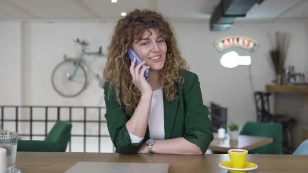 一位成年女性在咖啡馆里用智能手机 坐在桌旁开心地微笑着 自信地打电话交谈 — 图库视频影像