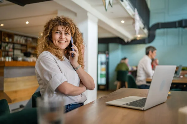 1人の女性大人Caucasian女性座ってカフェワークでノートパソコン電話話幸せな笑顔自信を持って笑顔本物の人のコピースペース — ストック写真