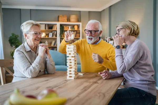 高齢者のグループ男性と女性の夫と妻の友人や家族は自宅でレジャーボードゲームをプレイ楽しい年金受給者の祖父と祖母は 成熟した娘と一緒に時間を過ごす — ストック写真