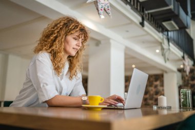 Kafe 'de oturup kendine güvenen mutlu bir gülüşü taklit ederken dizüstü bilgisayarda çalışan beyaz saçlı yetişkin bir kadın.
