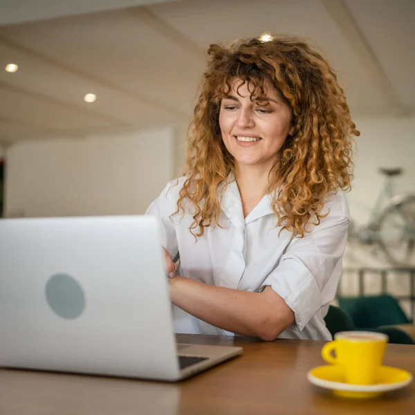 一人の女性大人Cucasian女性とともに巻き毛仕事上のラップトップコンピュータ上で座っている間にカフェ本物の人コピースペース幸せな笑顔自信 — ストック写真