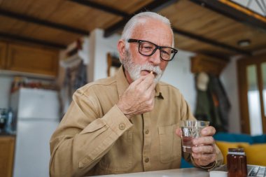 Kafkasyalı bir erkek büyükbaba evde oturur uyuşturucu tableti alır ağrı kesici içer ya da vitamin takviyesi alır. Etikette tıbbın gerçek insan sağlığı ve tıp kavramını okur.