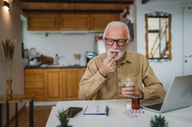 Kafkasyalı bir erkek büyükbaba evde oturur uyuşturucu tableti alır ağrı kesici içer ya da vitamin takviyesi alır. Etikette tıbbın gerçek insan sağlığı ve tıp kavramını okur.