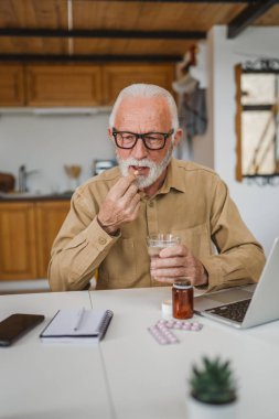 Kafkasyalı bir erkek büyükbaba evde oturur uyuşturucu tableti alır ağrı kesici içer ya da vitamin takviyesi alır. Etikette tıbbın gerçek insan sağlığı ve tıp kavramını okur.