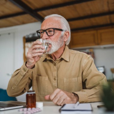 Kafkasyalı bir erkek büyükbaba evde oturur uyuşturucu tableti alır ağrı kesici içer ya da vitamin takviyesi alır. Etikette tıbbın gerçek insan sağlığı ve tıp kavramını okur.