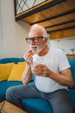 Kafkasyalı bir erkek büyükbaba evde oturur uyuşturucu tableti alır ağrı kesici içer ya da vitamin takviyesi alır. Etikette tıbbın gerçek insan sağlığı ve tıp kavramını okur.
